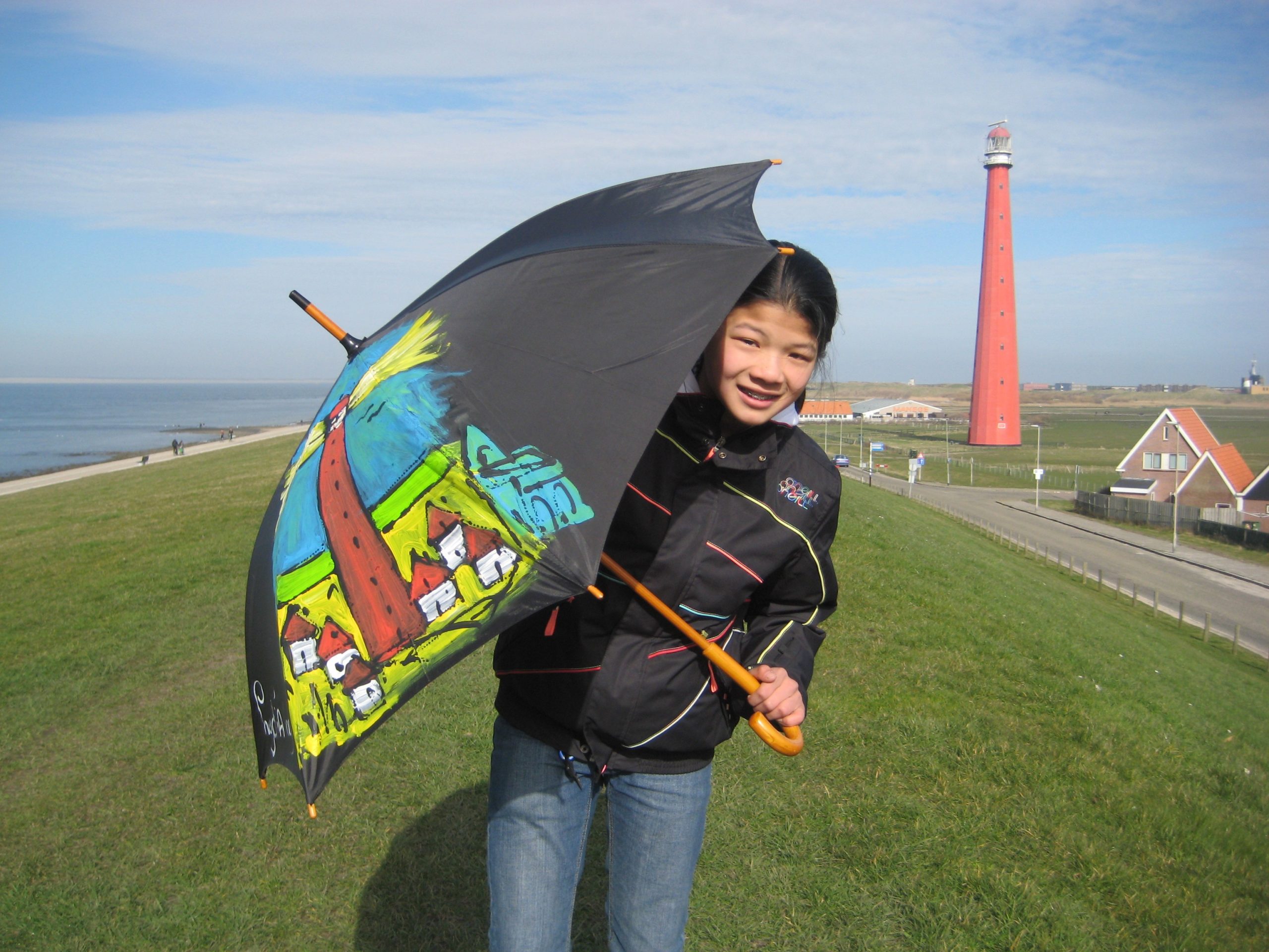 Jongen met paraplu op een dijk. Op de achtergrond een vuurtoren.